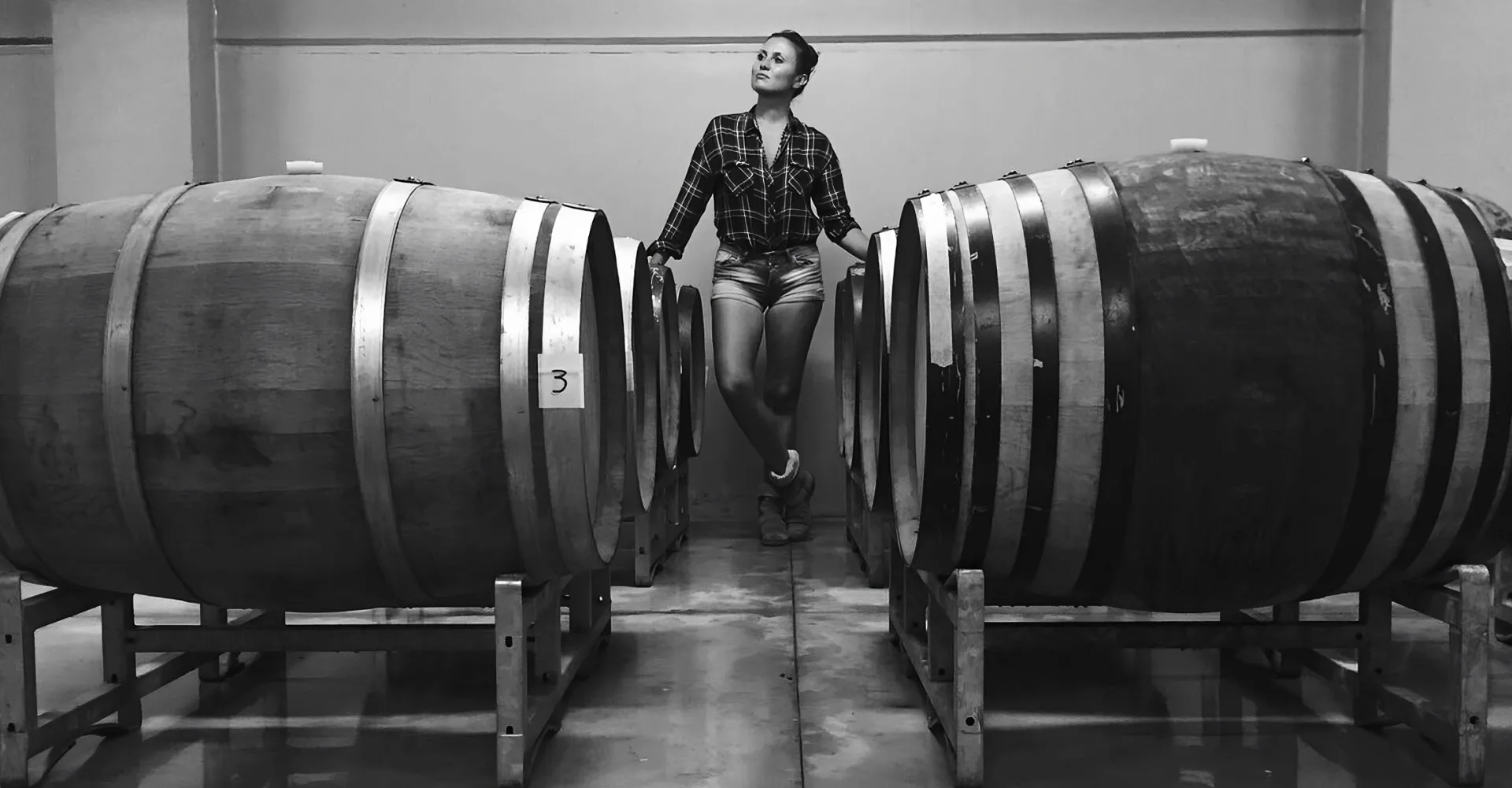 Augusta Bargilli seduta tra due botti in cantina, in bianco e nero