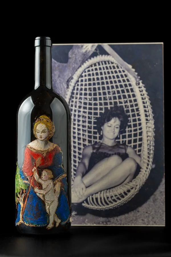 Il magnum dipinto con la Madonna accanto a una fotografia in bianco e nero di una giovane donna seduta in una poltrona di vimini