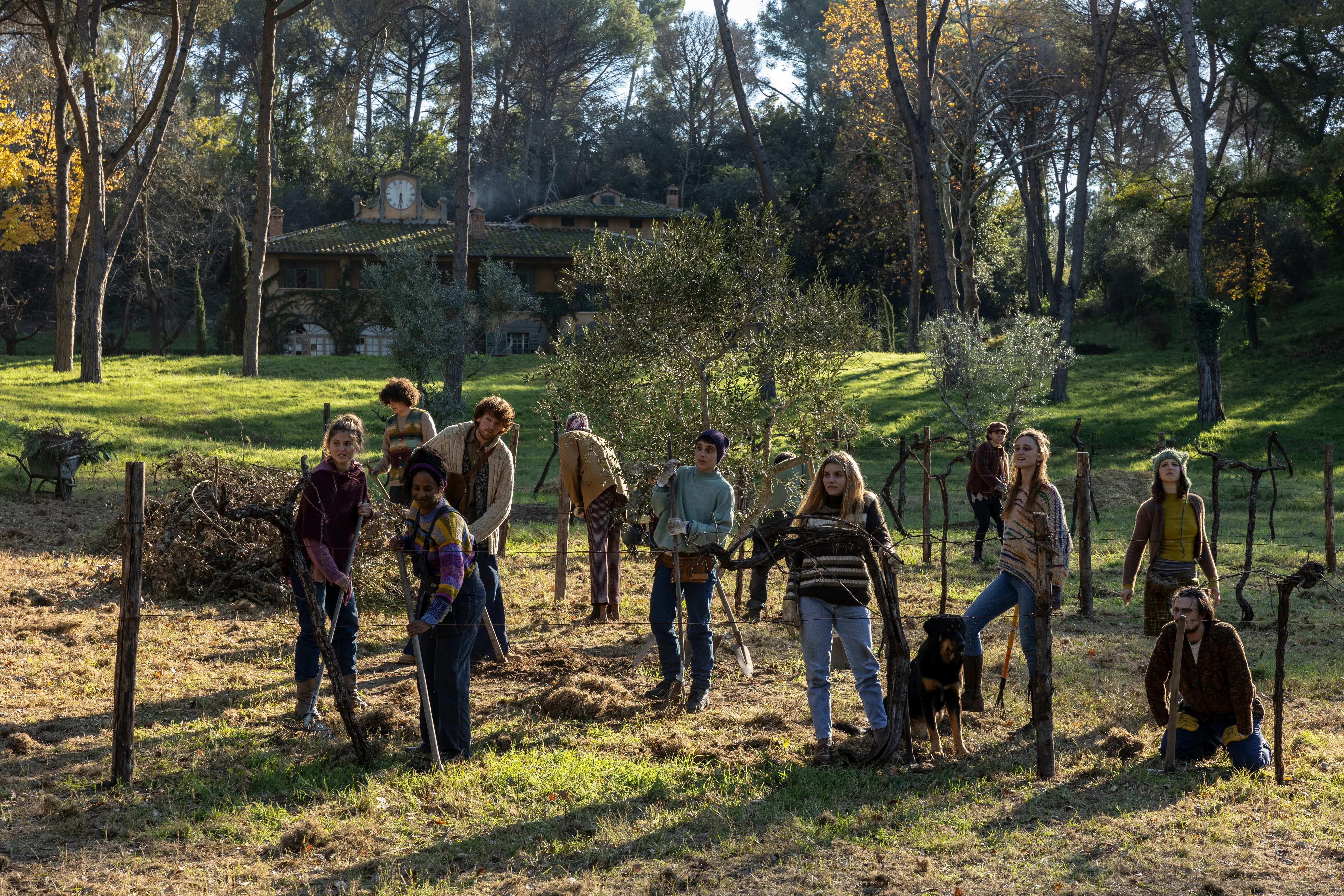 Una scena di Cinque secondi: ragazze e ragazzi lavorano la terra tra vecchie viti e ulivi, con zappe e vanghe; dietro di loro un prato e una villa con l’orologio sul tetto, tra i pini