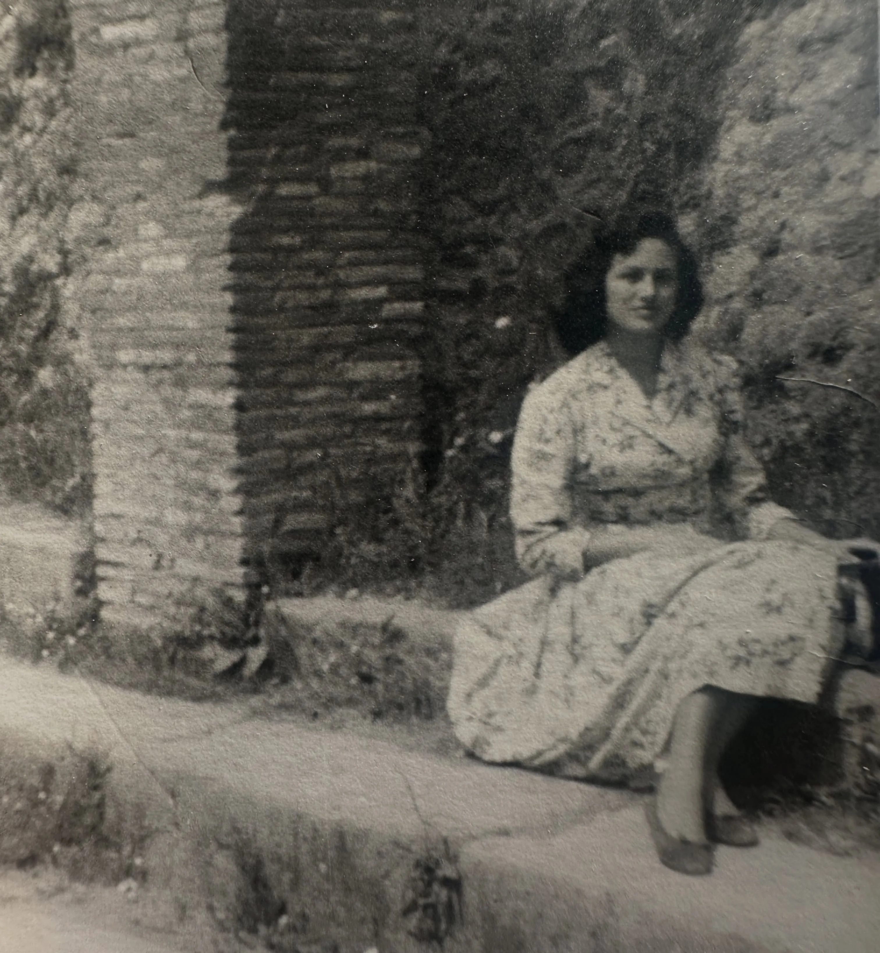 Una fotografia in bianco e nero di Maria Teresa, la madre di Augusta, da giovane, seduta su un muretto in un abito a fiori